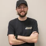 Tyler poses with arms crossed for Heavenly Garage Doors against a gray background